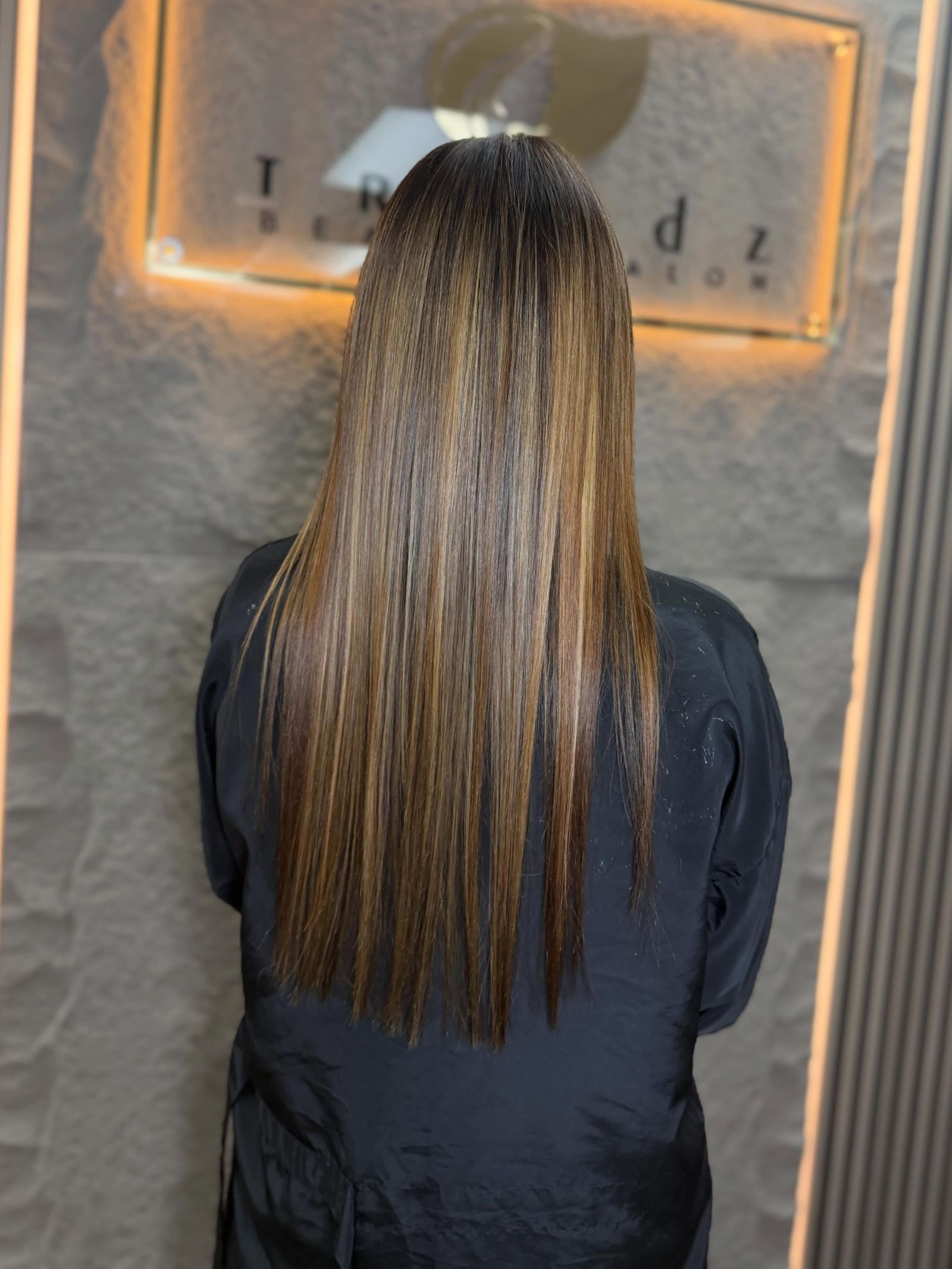 Client showing off a fresh balayage hairstyle in front of the glowing Trendz Beauty Salon sign